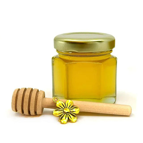 Small jar of honey with gold flower charm and wooden honey dipper on white background