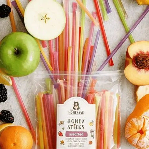 Honey Sticks spilling out of the bag and onto a white surface with apples oranges and other fruit