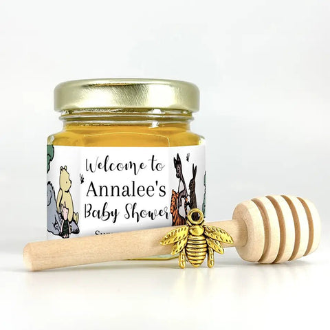 Small jar of honey with personalized Winnie the Pooh label, gold bee charm, and wooden honey dipper on white background