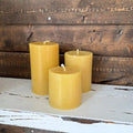 Three yellow candles on a wooden surface with a rustic background