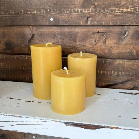 Three yellow candles on a wooden surface with a rustic background