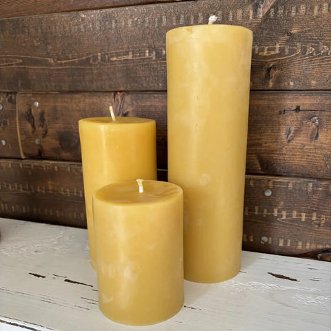 Three yellow candles of different sizes on a wooden surface with a rustic background.