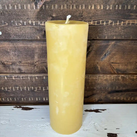 Yellow beeswax candle on a wooden surface with a rustic background