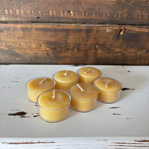 Set of six yellow candles in clear glass holders on a wooden surface