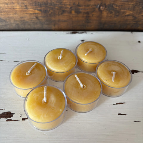 Six small yellow candles in clear holders on a wooden surface