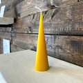 Yellow cone-shaped beeswax candle sitting on wooden surface