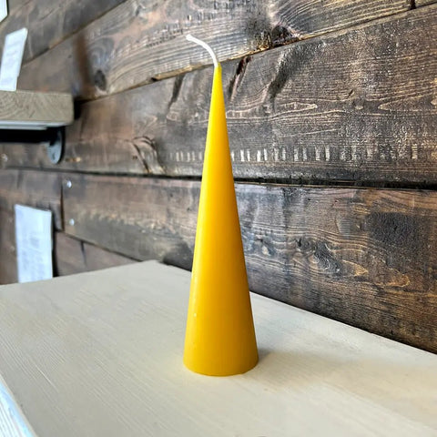 Yellow cone-shaped beeswax candle sitting on wooden surface
