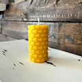 Yellow beeswax candle with hexagon shapes on it sitting on a wooden surface