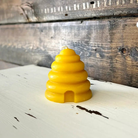 Yellow beehive-shaped beeswax candle sitting on wooden surface