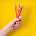 Hand holding colorful straws against a yellow background