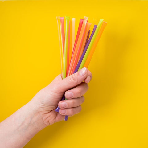 Hand holding colorful straws against a yellow background