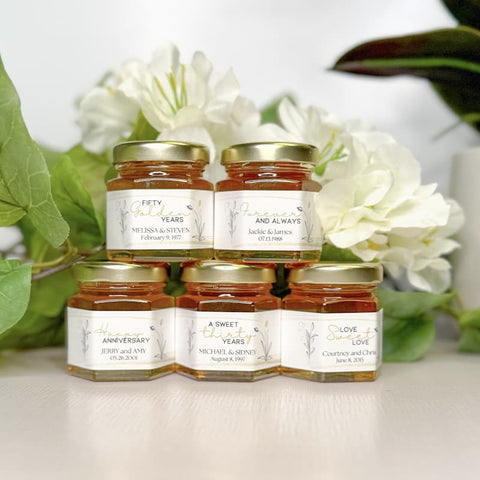 Jars of honey with personalized labels on a white surface with flowers in the background