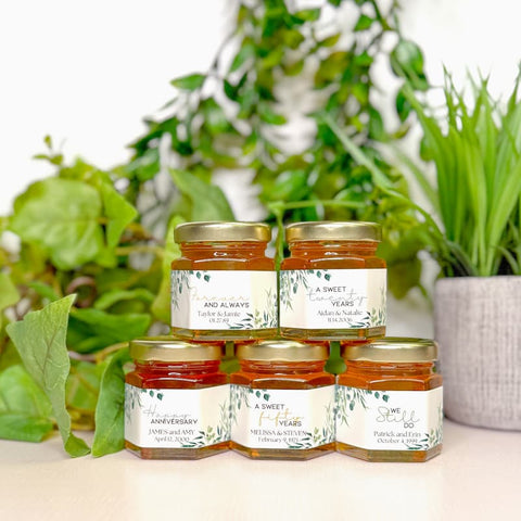 Jars of honey with labels on a surface with plants in the background
