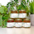 Five jars of honey with personalized labels on a white surface with greenery in the background