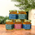Five jars of honey with personalized labels on a wooden surface.