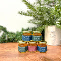 Set of small jars with labels on a wooden surface with greenery in the background