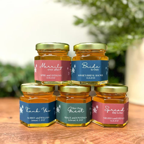 Five jars of honey with personalized labels on a wooden surface with a blurred green background.
