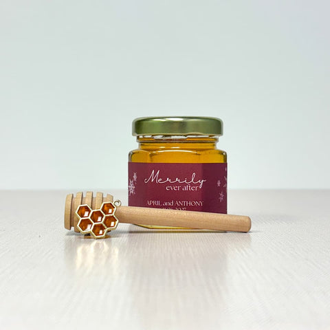Jar of honey with a decorative label, honeycomb charm, and a honey dipper on a white background