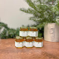 Jars of honey stacked on a wooden surface with a blurred green plant in the background