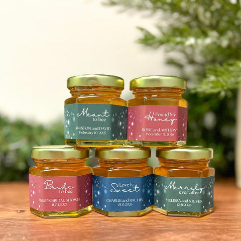 Five jars of honey with personalized labels on a wooden surface with a blurred natural background.