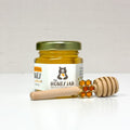 Honey jar with a honey dipper and honeycomb charm on a white background