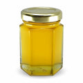 Hexagonal glass jar with gold lid filled with a yellow substance on a white background