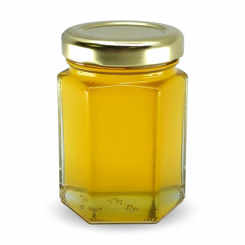Hexagonal glass jar with gold lid filled with a yellow substance on a white background