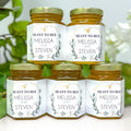Five jars of honey stacked in a pyramid formation with personalized labels on a white surface.