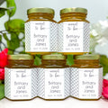 Five jars of honey with personalized labels on a white background with flowers.