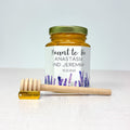Honey jar with personalized label and wooden honey dipper on a light background