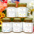 Five jars of honey with personalized labels against a floral background