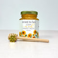 Honey jar with floral label and honey dipper on a white background