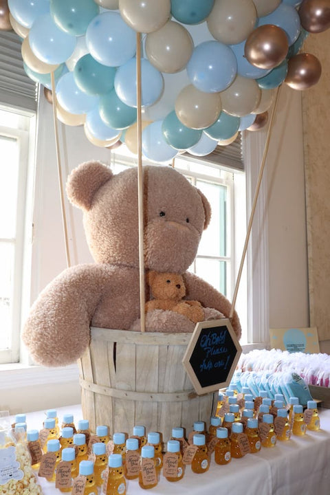 Decorative setup with balloons, teddy bears, and small bear-shaped honey bottles on a table.