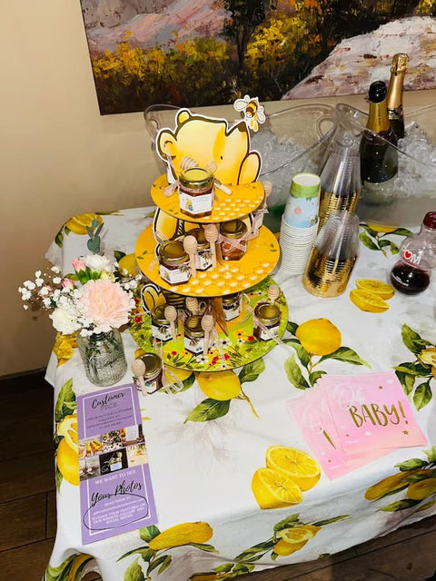 Decorative table setting with a lemon-themed tablecloth, cake stand, and baby shower decorations.