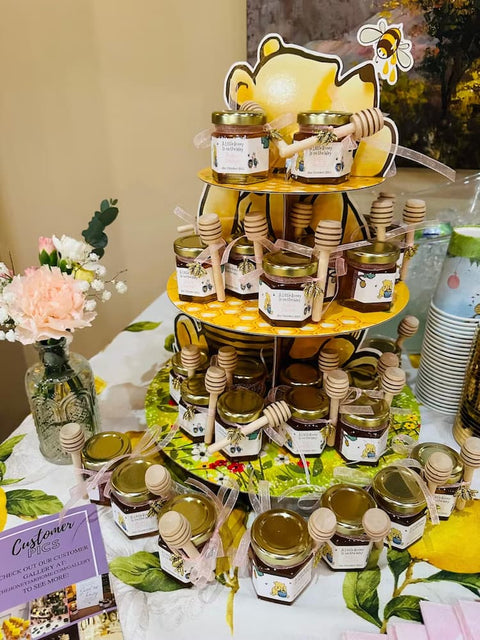 Three-tiered stand with jars of honey on a table with floral decorations
