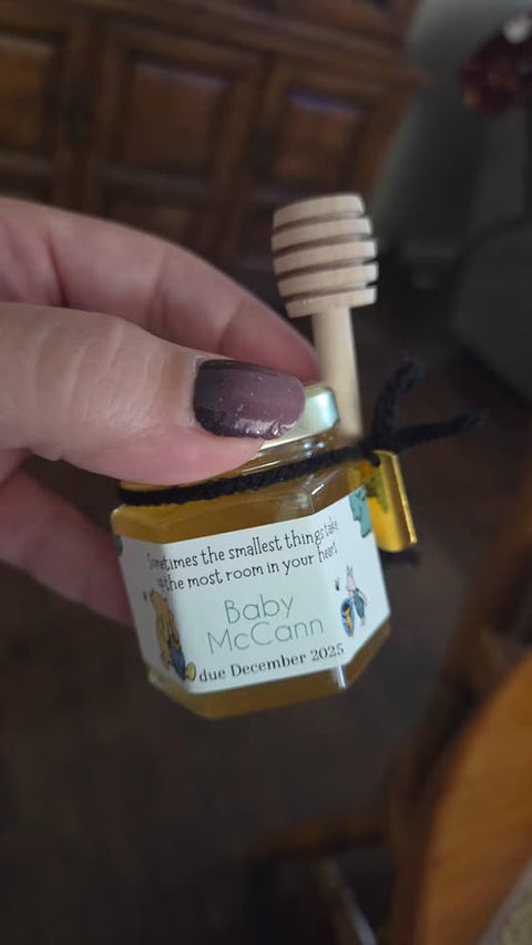 Small jar of honey with a personalized label held by a hand, with a wooden honey dipper in the background.
