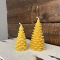 Two yellow tree-shaped candles on a wooden surface with a rustic background