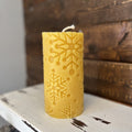 Yellow candle with snowflake pattern on a rustic wooden surface
