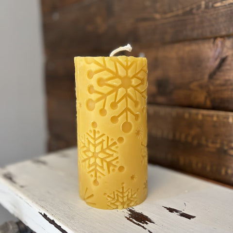 Yellow candle with snowflake pattern on a rustic wooden surface