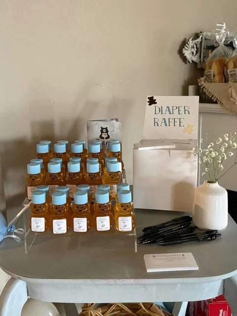 Table with baby bottles, pens, and a 'Diaper Raffle' sign in a neutral setting.