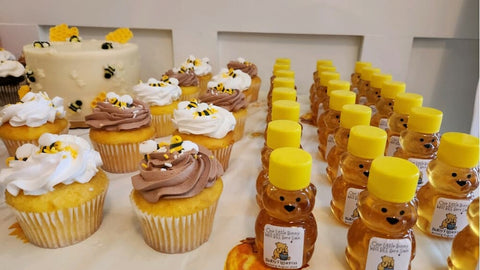 Cupcakes with honeycomb decorations and small bear-shaped honey jars on a white surface.