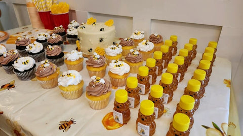 Table with cupcakes, a cake, and small honey jars on a white surface.