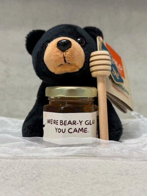 Stuffed bear with a jar of honey and a honey dipper on a white surface
