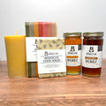 Honey jars, beeswax food wrap, and a candle on a wooden surface with a white background