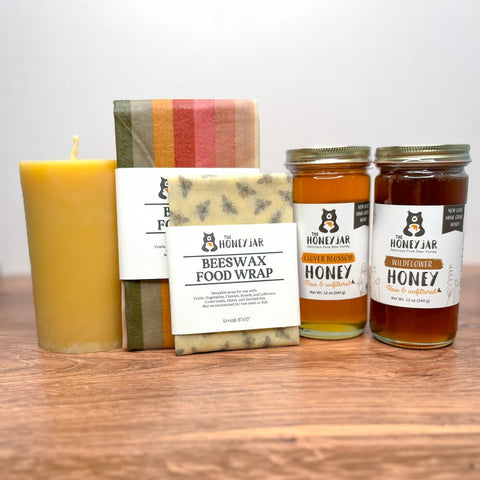 Honey jars, beeswax food wrap, and a candle on a wooden surface with a white background