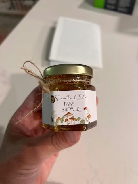 Hand holding a small jar with a 'Baby Shower' label against a neutral background