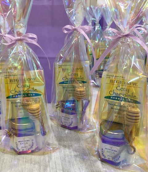 Tea package with honey dipper and honey jar in a cellophane bag on a textured surface.
