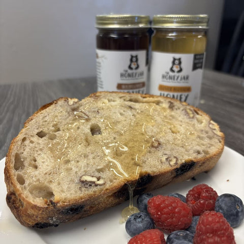 Toast with honey, berries, and jars of honey in the background.