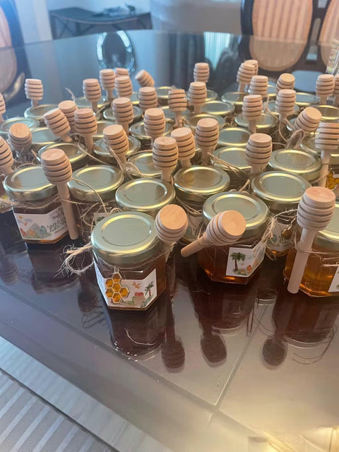 Jars of honey with wooden honey dippers and honeycomb charms on a reflective surface