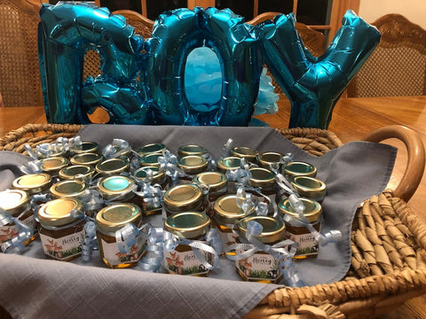 Jars of honey with decorative ribbons on a tablecloth, surrounded by blue 'BOY' balloons.